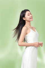 Woman in a white slip dress with flowing hair enjoying a moment of joy against a green background.