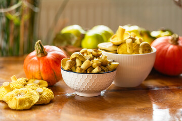 Bowl of fresh honey mushrooms with autumn fruits and pumpkin on wooden table