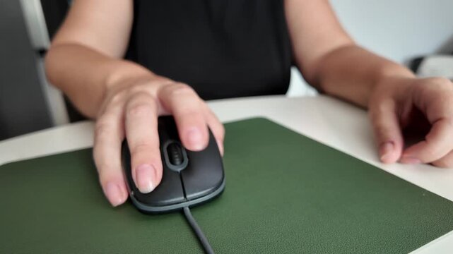 Woman using a mouse on a mouse pad and desk, detail of a modern working environment
