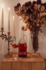 Homemade cherry liqueur with candles and dried roses on a rustic wooden table