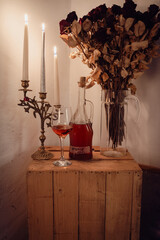 Homemade cherry liqueur with candles and dried roses on a rustic wooden table