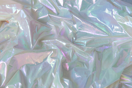 Shiny holographic fabric with smooth folds and iridescent light reflections. Abstract background with metallic texture and soft pastel colors.