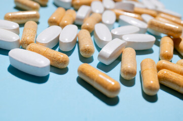 White and beige oval vitamin tablets close-up on blue background. Concept of health and medicine, pharmacology, pharmacy, healthcare. Antibiotic or dietary supplement macro background