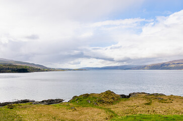 Isle of Mull - Peaceful coastal scene with calm water, rocky shore, and distant hills beneath a dramatic cloudy sky.