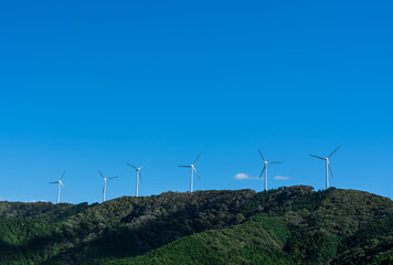 A spectacular landscape where multiple white wind turbines are lined up on a green mountain ridge...
