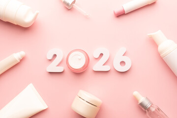 Best skincare products and cosmetic trends of 2026 concept. 2026 white number with lip balm, cream bottle, serum and lotion on pink background.
