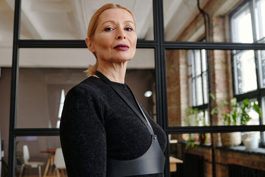 Low angle medium portrait of modern senior Caucasian woman with stylish goth makeup on face standing in loft office looking at camera