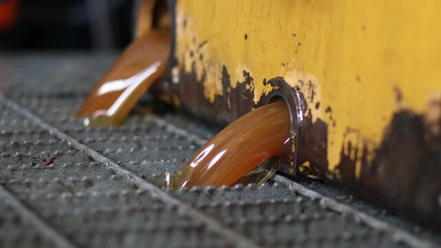 High-viscosity, brown fluid being drained from the circular opening of a transmission, flowing over a metal grate in a service bay.