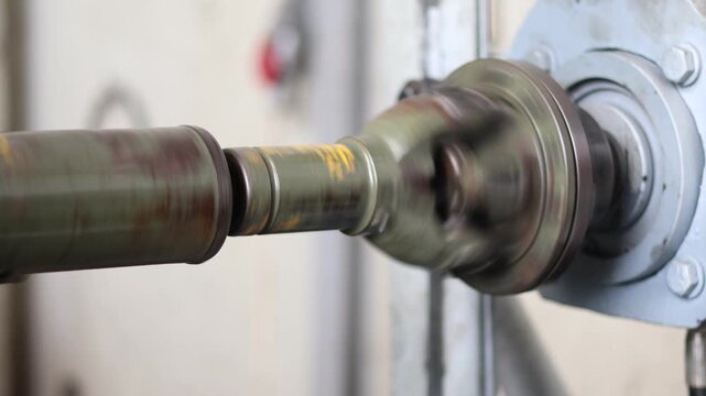 High-speed rotating industrial driveshaft or power transmission element in motion, with visible wear and lubrication residue on the metal surface.