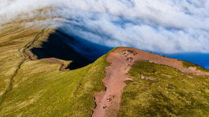 Aerial drone view of hikers on a mountain path above a dramatic cloud inversion in Wales