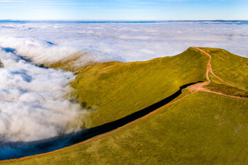 Panoramic mountain landscape with a hiking path above a sea of clouds and fog.