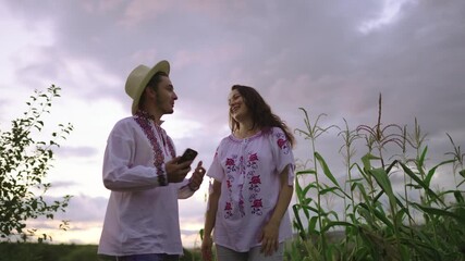 Romanian couple in traditional clothes taking a selfie in a field with a cloudy sky at sunset - Powered by Adobe