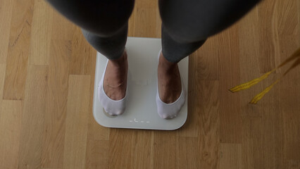 Woman Measuring Body Weight On Weighing Scale At Home. Close up of a woman legs measuring weight with scale at home. 