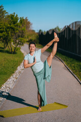 Naklejka premium Woman striking an elegant standing yoga pose on a sunlit path, exemplifying flexibility, focus, and grace in harmonious outdoor setting.