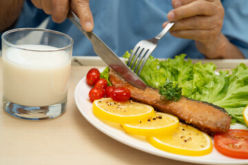 Asian elderly woman patient eating salmon stake and vegetable salad for healthy food in hospital.