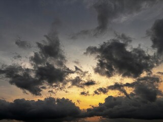 Obraz premium Dramatic sunset sky with dark storm clouds and a warm orange glow on the horizon, creating a powerful contrast between light and shadow in the evening atmosphere.