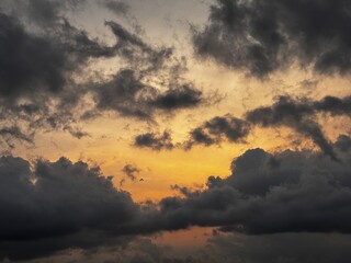 Fototapeta premium Dramatic sunset sky with dark storm clouds and a warm orange glow on the horizon, creating a powerful contrast between light and shadow in the evening atmosphere.