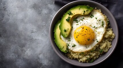 A healthy breakfast bowl filled with quinoa a fried egg sliced avocado and garnished with fresh herbs and pepper