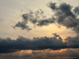 Obraz premium Dramatic sunset sky with dark storm clouds and a warm orange glow on the horizon, creating a powerful contrast between light and shadow in the evening atmosphere.