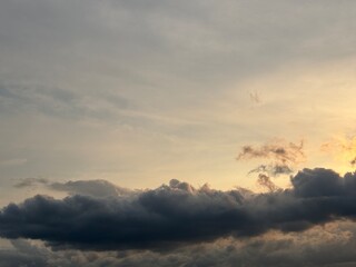 Obraz premium Dramatic sunset sky with dark storm clouds and a warm orange glow on the horizon, creating a powerful contrast between light and shadow in the evening atmosphere.