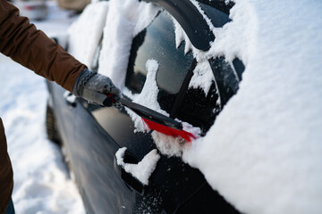 Cleaning car from snow on a winter day. Scraping ice from the car window