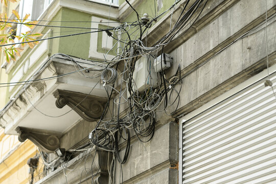 Tangled network and power cables attached to a historic urban facade showing outdated telecom wiring and poor infrastructure maintenance in city environment