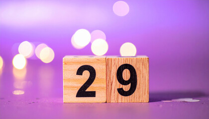 Wooden cubes with number 29 with confetti, purple bokeh light. Celebration mood.