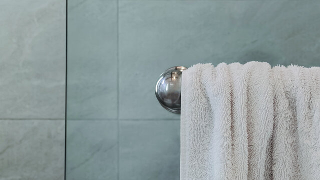 Clean white towel hanging on metal bar in a modern bathroom with tile wall, minimal design and hygiene lifestyle concept, spa or hotel interior.