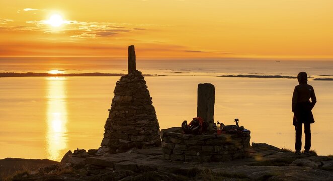 Silhouette of a woman watching the sunset next to cairns, Rørsethornet stone staircase, with 3292 steps one of the longest continuous stone staircases in the world, Sherpatreppe or Midsundtreppe or Midsundtrappene, Rørsethornet hike, Otroya or Otrøya island, Møre og Romsdal, Norway