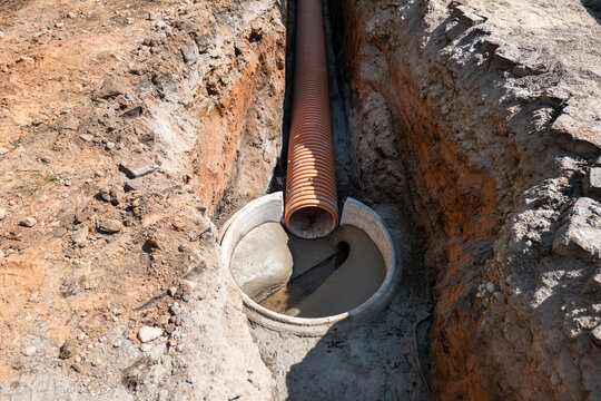 Instala&ccedil;&atilde;o subterr&acirc;nea de tubo corrugado Marrom numa vala de terra com liga&ccedil;&atilde;o a uma boca de manilha circular de bet&atilde;o com argamassa fresca