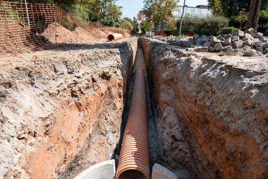 Vala profunda aberta em solo avermelhado com instala&ccedil;&atilde;o de tubula&ccedil;&atilde;o corrugada de grande di&acirc;metro para obras de infraestrutura subterr&acirc;nea de saneamento p&uacute;blico numa &aacute;rea urbana