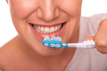Close-up of a woman smiling while brushing her teeth with a blue toothbrush, representing dental hygiene and oral care routine.