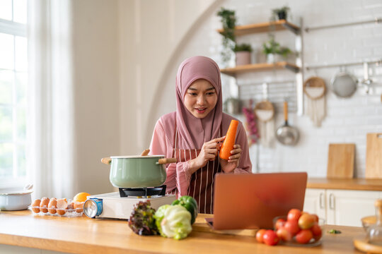 Muslim woman vlogger live streaming cooking online in kitchen look at camera with vegetables, content creator culinary class at home studio, halal food influencer cooking live, video for social media - Powered by Adobe