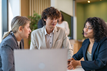 Diverse tech team meeting on software project, mentor guiding coworker on laptop, teamwork...