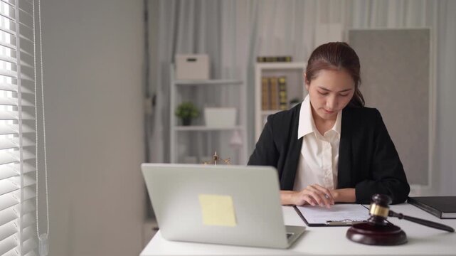 Asian legal professional drafting important documents conducting online research using laptop computer at modern office for legal work