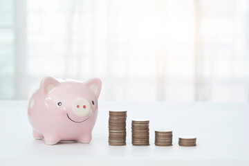 Piggy bank and stack of coins on white tabletop and blurred background. Finance and money saving concept.
