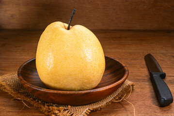 Single juicy ripe chinese pear or Pyrus pyrifolia in wooden dish placed on sackcloth with knife on wooden tabla.