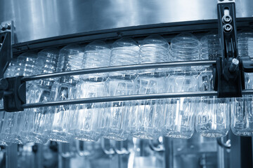 The  empty drinking water bottles  hanging on the overhead conveyor belt for filling process in the light blue scene.