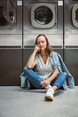 Woman sitting on floor in self service laundromat while waiting laundry
