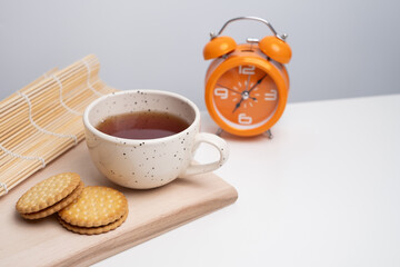 Cup of tea, notebook, cookies, and clock on light desk surface. Symbol of coffee break, productivity, time management, or working day routine.