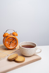 Cup of tea, notebook, cookies, and clock on light desk surface. Symbol of coffee break, productivity, time management, or working day routine.