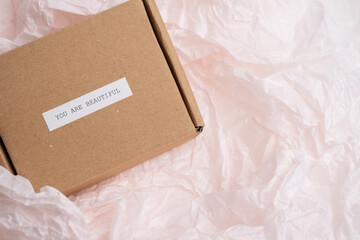 Gift box with the motivational quote "You are beautiful" on wrinkled pink tissue paper. Eco-friendly packaging, self-care, gift-giving, and a message of beauty and love.