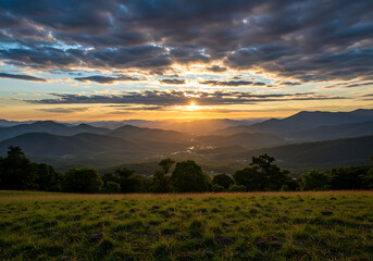 A dramatic golden sunset with sunbeams breaking through clouds over a vast mountain valley and grassy meadow.