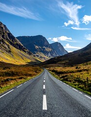 Naklejka premium Asphalt road stretches between mountains toward a clear blue sky with a few clouds