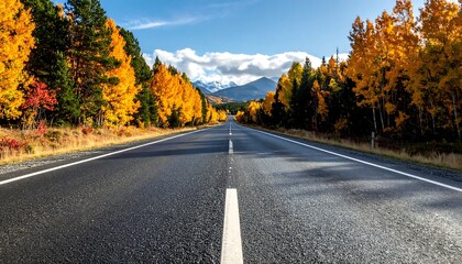 Fototapeta premium Asphalt road stretches through vibrant autumn trees towards snow-capped mountains under a blue sky