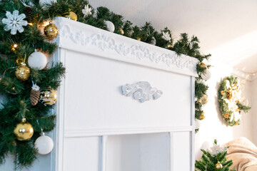 Christmas garland of green fir with gold and white balls on the fireplace in the bright living room