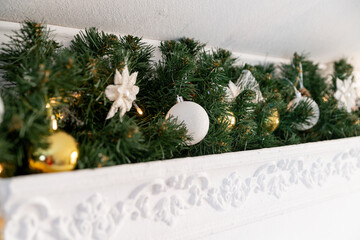 Christmas garland of green fir with gold and white balls on the fireplace in the bright living room