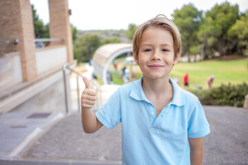 Cute little boy wearing blue polo shirt smiling tho camera showing thumb up at at golf course.