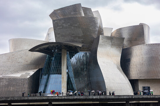 Bilbao, Spain &ndash; Nov 21, 2021: People with umbrellas walk in front of the Guggenheim Museum Bilbao, a famous landmark of deconstructivist architecture designed by architect Frank Gehry.