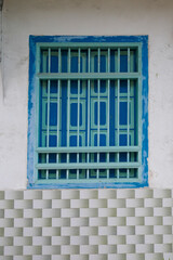 Traditional wooden window painted in shades of turquoise and blue, framed with vertical bars and set against a wall finished with light green and white ceramic tiles on a heritage shophouse, Penang.